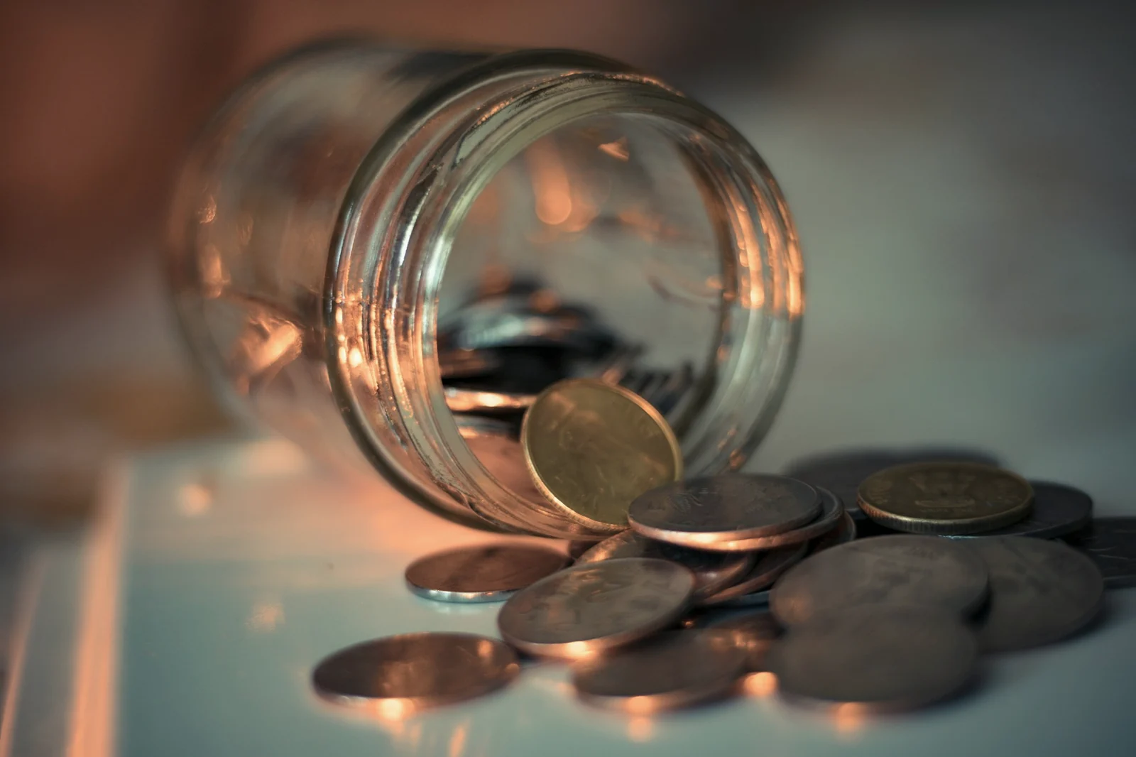 Indian rupee coins spilling from a glass savings jar